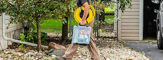 man carrying an Adrian Steel portable parts case and a yellow cable with his left arm as he walks through a garden