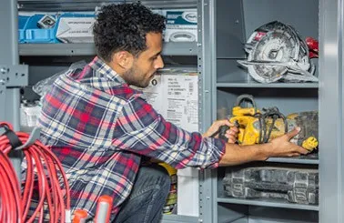 man placing a work tool in an Adrian Steel locker filled with various work tools installed in the interior of a work van