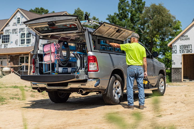 a man taking a portable part case from a pickup truck fully upfitted with Adrian Steel pickup equipment