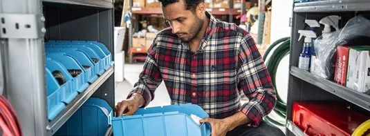 man in a warehouse placing an Adrian Steel portable bin full of parts in a shelf filled with other similar containers