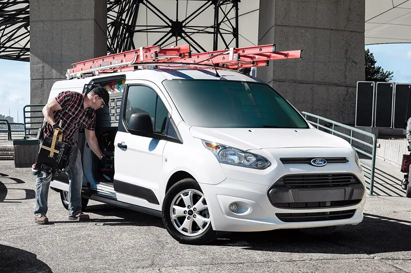 man picking up some work tools from the interior of a Ford Transit Connect upfitted by Adrian Steel